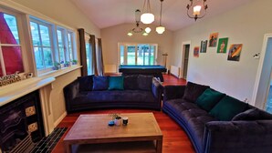 Ein Wohnzimmer mit Kamin, zwei dunklen Sofas, einem Holztisch und einem Billardtisch im Hintergrund.