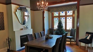 Ein Esszimmer mit Holztisch, Stühlen, einer Chandelier, einem Weihnachtsbaum und einem großen Fenster mit Buntglas.
