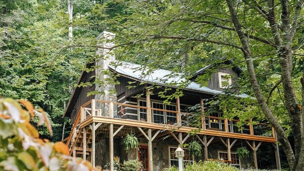 Un rustico chalet con veranda in legno e numerose finestre, immerso in una fitta foresta.