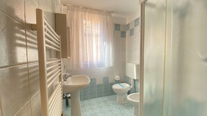 A bathroom with a radiator, a sink, a toilet, and a window with a curtain. - Appartamento Adriana 3 - Carraro Immobiliare Jesolo (Lido di Jesolo)