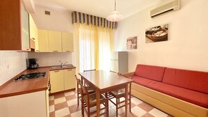 A compact kitchen with a dining table, chairs, a red sofa, and a checkered floor. - Appartamento Adriana 3 - Carraro Immobiliare Jesolo (Lido di Jesolo)