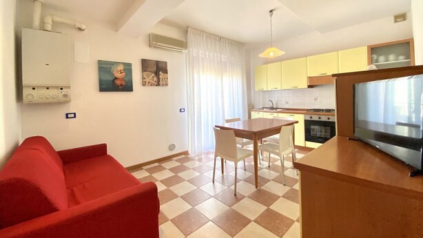 Un espacio habitable compacto con kitchenette, una zona de comedor con mesa y sillas, un sofá rojo y una televisión.