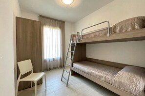 Een slaapkamer met een stapelbed, een witte stoel en een raam met gordijnen.