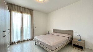 A bedroom with a bed, nightstand, and wardrobe. - Appartamento Treporti 4 Cavallino- Carraro Immobiliare Jesolo (Cavallino)