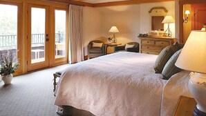 Une chambre d’hôtel avec un grand lit, un bureau, une chaise, une commode et un balcon avec des rideaux.