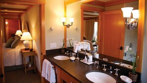 Une salle de bain d’hôtel équipée d’un double lavabo, d’un miroir, d’un porte-serviettes et d’une table de chevet avec une lampe.