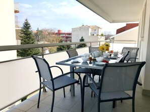 Un balcón con mesa dispuesta para comer, sillas y un florero con flores.