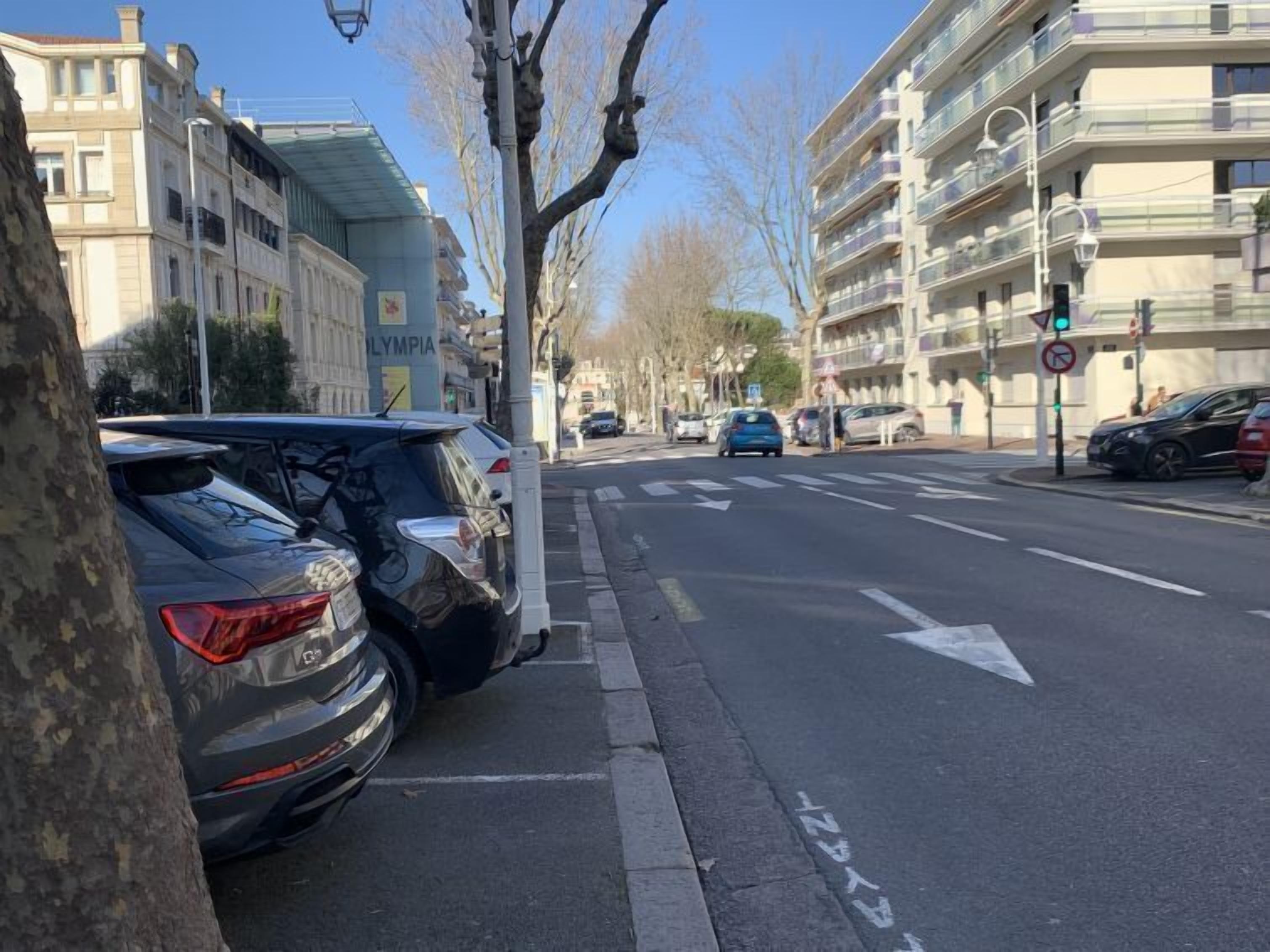 Vista de la calle con coches estacionados, un edificio con el rótulo 'OLYMPIA' y un cielo despejado.