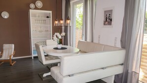 Ein modernes Wohnzimmer mit einem weißen Sofa, einem runden Esstisch und einer weißen Kommode mit Gläsern.