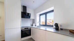 A modern kitchen with white cabinets, a built-in oven, a coffee maker, and a window providing a view of the cityscape.