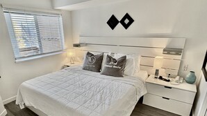 Ein ordentlich eingerichtetes Schlafzimmer mit einem großen Bett, Nachttischen, einer Nachttischlampe, einer Vase und einer Wandleuchte.