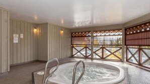Ein Whirlpool mit Fliesenboden und Metallgeländern, umgeben von Holzwänden und einem Blick durch ein Gitterfenster.