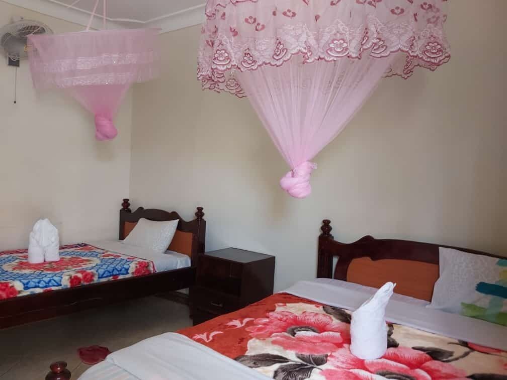 Een hotelkamer met twee bedden, elk voorzien van een bloemenprint deken en een roze hemelbed.