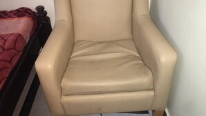 Un sillón color arena con estructura de madera, ubicado frente a una pared de tonos claros.