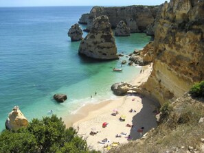 A coastal beach with clear turquoise water, rocky cliffs, and a sandy shore with people and umbrellas. - Villa Quinta do Sol by Interhome (Armação de Pêra)