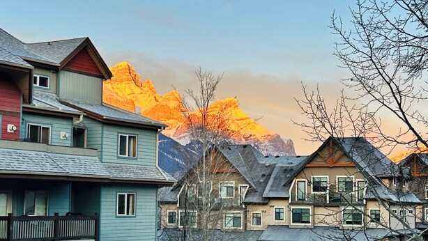 A row of multi-story buildings with balconies, set against a backdrop of mountains during sunset. - SUNNY BRIGHT King Bed Suite Full Kitchen Free Parking Balcony BBQ Gym (Canmore)
