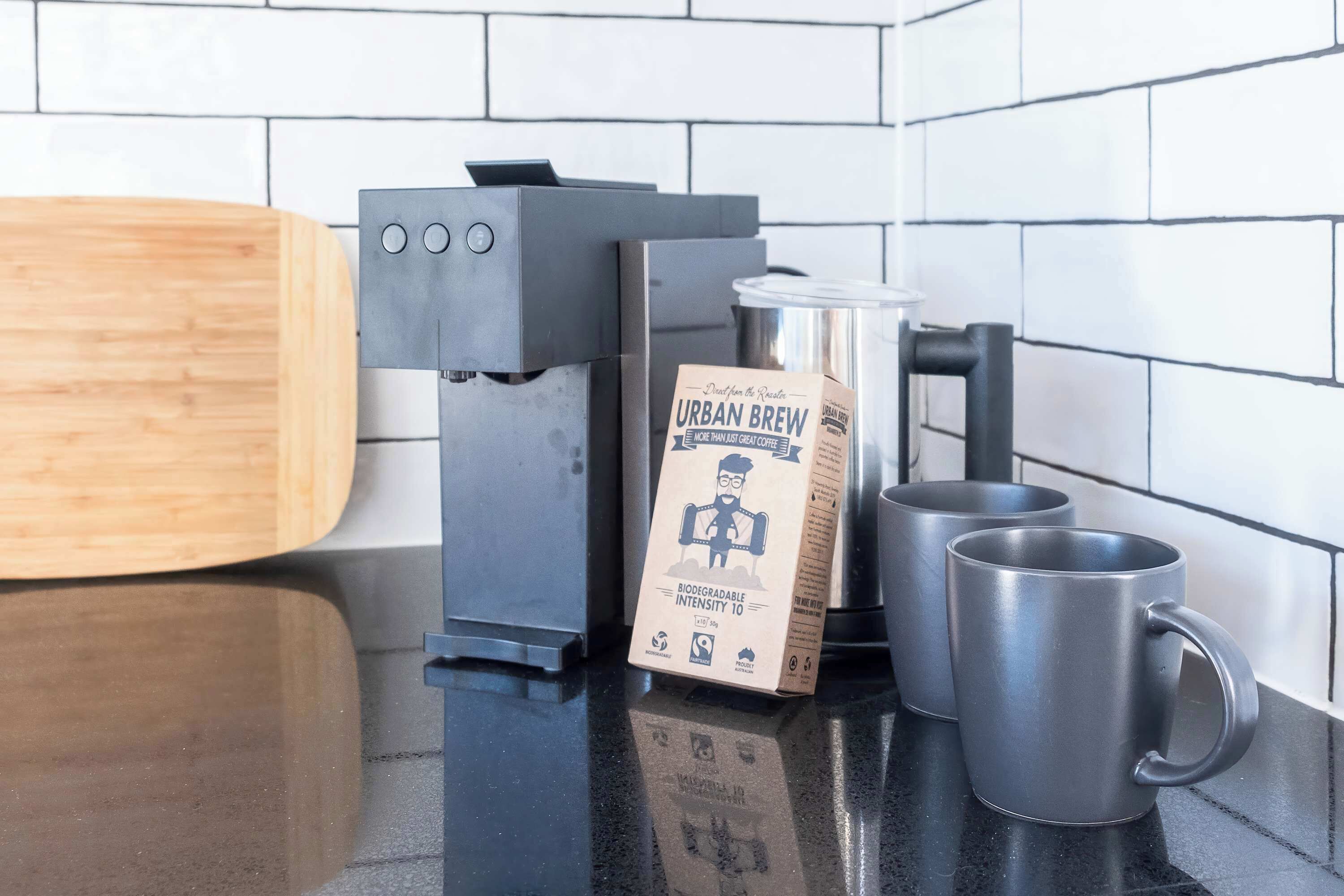 A coffee machine, a box of Urban Brew coffee, and two metal mugs on a kitchen counter.