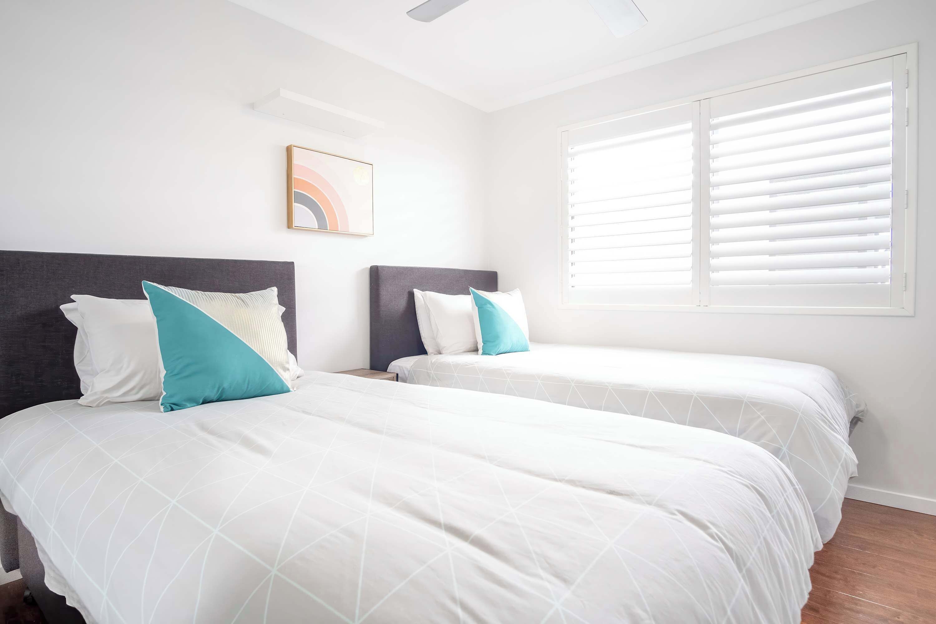 A hotel room with two beds, a ceiling fan, a window with blinds, and a framed picture on the wall.