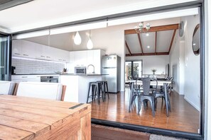 A modern kitchen with white cabinets, a central island, and bar stools. - Warana Abode - Pool, Studio & Walk to Beach (Warana)