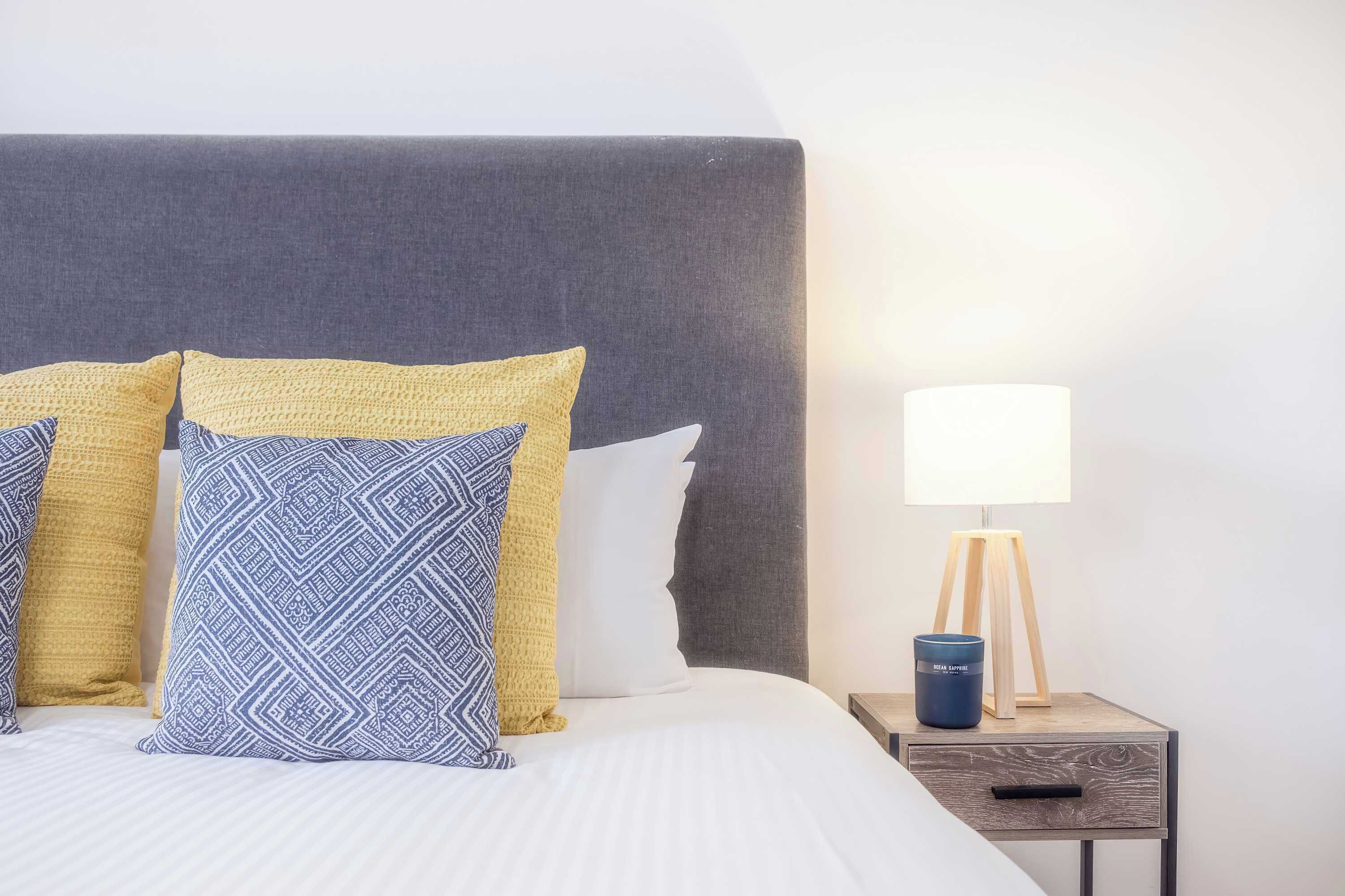 A neatly made bed with patterned pillows, a bedside lamp, and a small wooden nightstand.