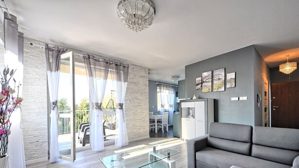 Ein modernes Wohnzimmer mit grauem Sofa, einem Glastisch und einem Essbereich mit weißem Tisch und Stühlen.