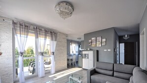 Ein modernes Wohnzimmer mit Glastisch, grauem Sofa und einem Essbereich im Hintergrund.