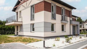Ein modernes, zweistöckiges Haus mit Balkon, großen Fenstern und einer flachen Dachkonstruktion.
