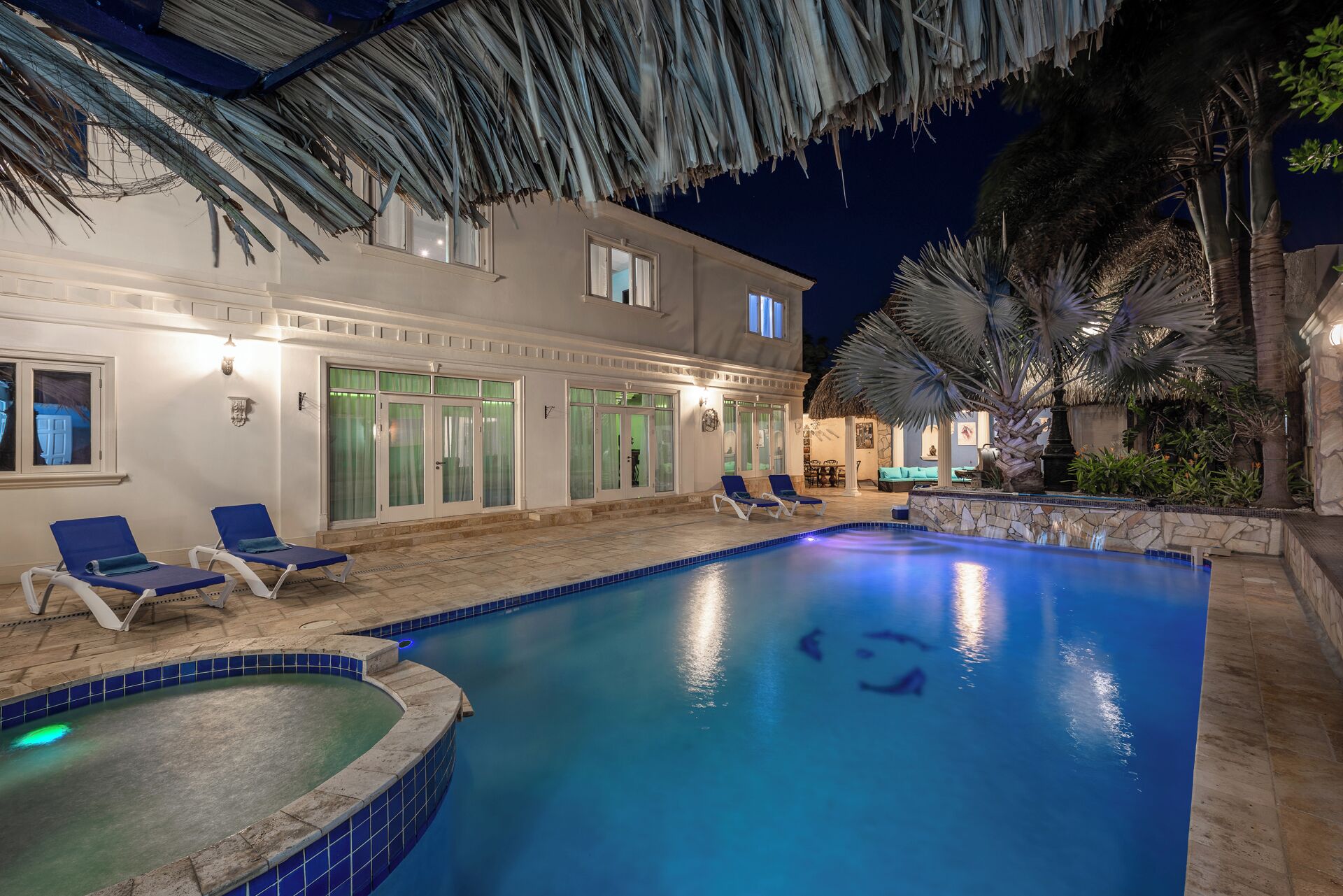 A pool area with lounge chairs, a hot tub, and a well-lit building with large windows.