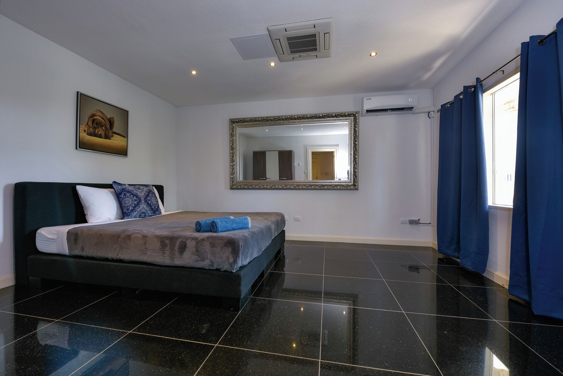 Camera d'albergo con un letto, uno specchio grande, un condizionatore d'aria e una finestra con tende.