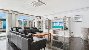 A modern living room with a black leather sofa, a wooden coffee table, and a flat-screen TV. There are glass cabinets with decorative items and a large stone planter. - Aruba luxury villa La Casa Piu Bella your home away from home (Noord)