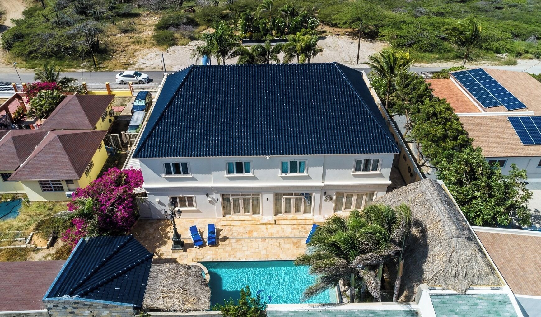 Une maison à deux étages dotée d’une piscine, de panneaux solaires et d’un toit de chaume.