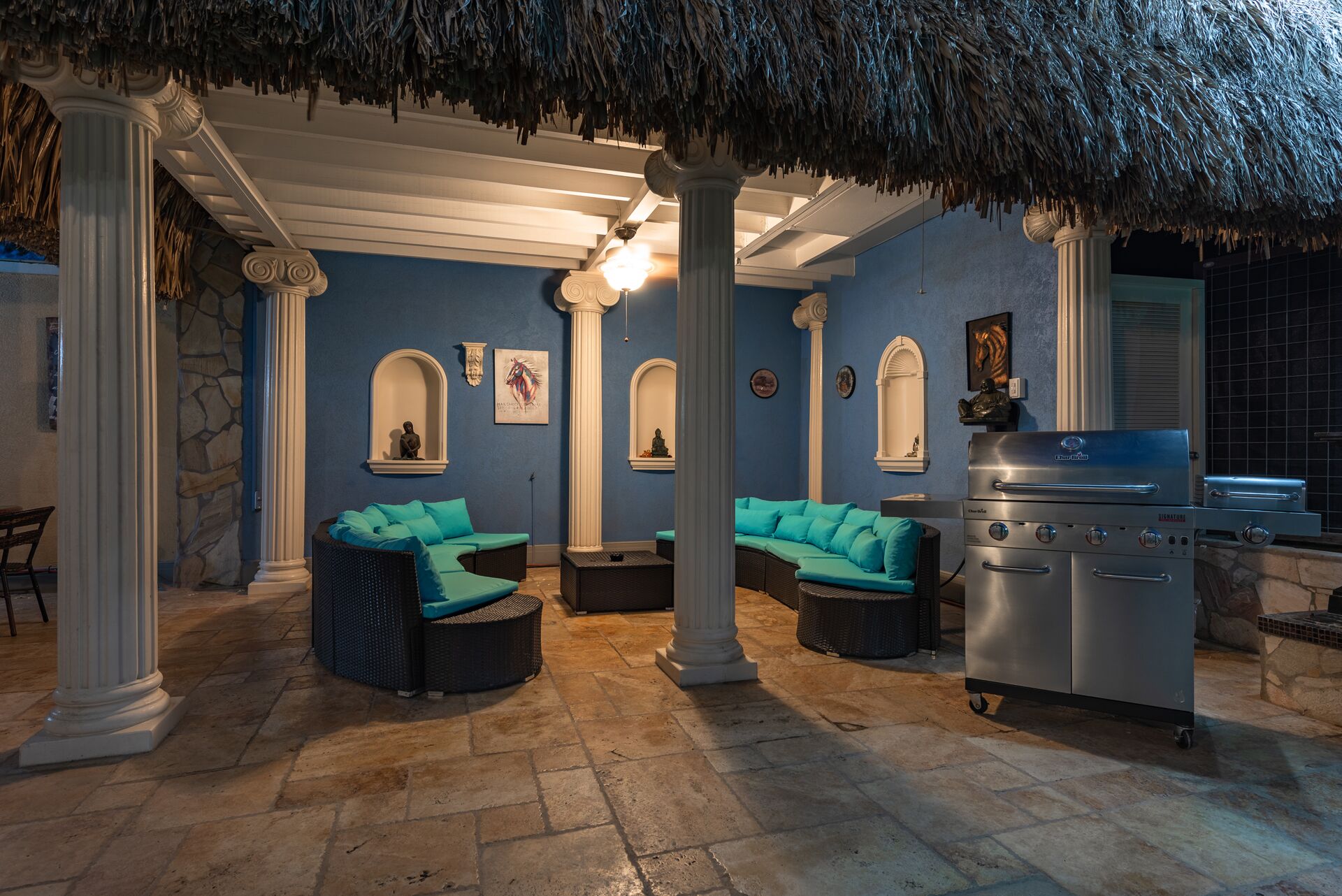 A covered outdoor seating area with two sofas and a grill.