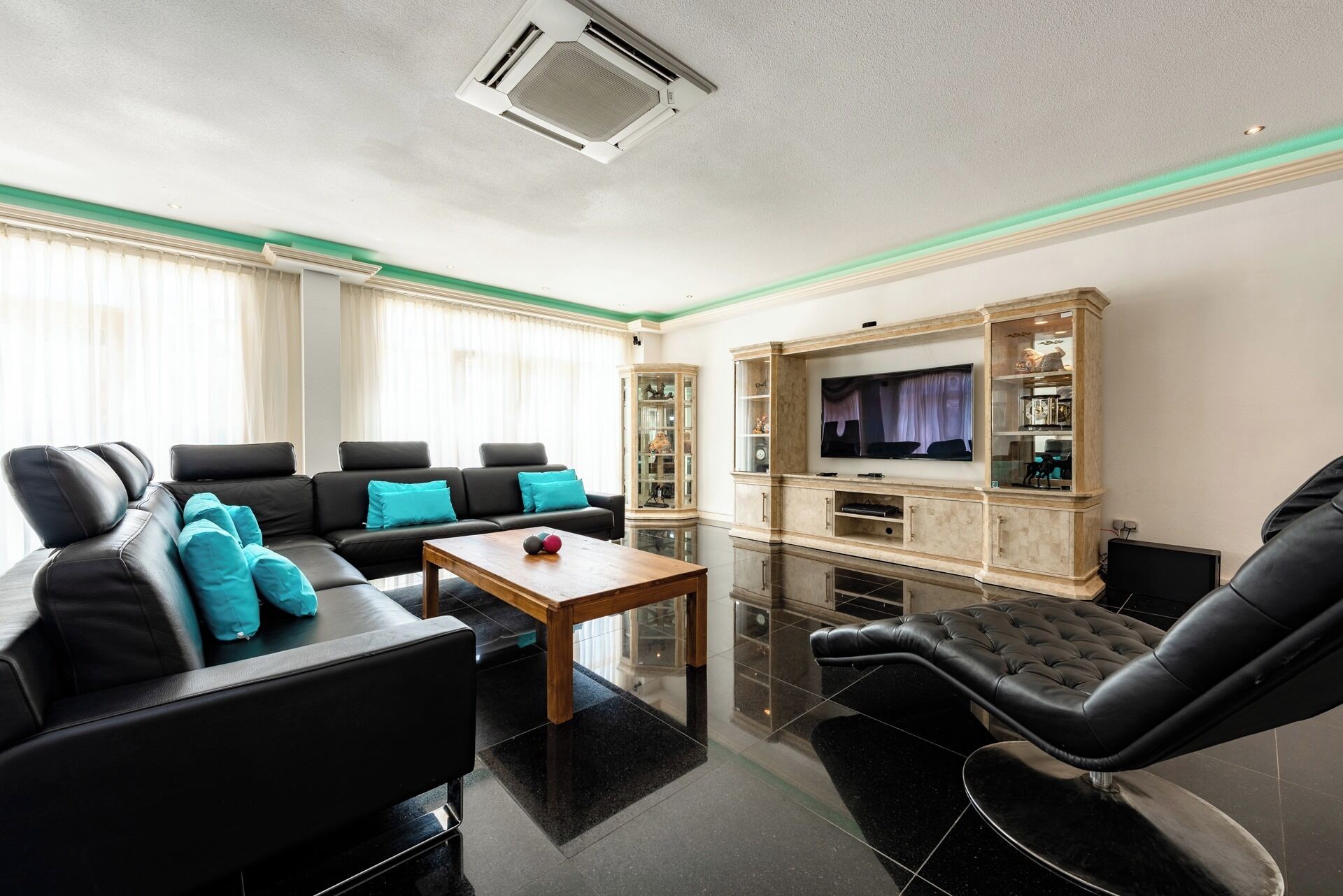 A modern living room with a black leather sofa, a wooden coffee table, and a TV on a wooden cabinet.
