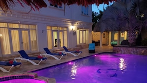 A swimming pool with lounge chairs and a hot tub, surrounded by a stone wall and palm trees. - Aruba luxury villa La Casa Piu Bella your home away from home (Noord)