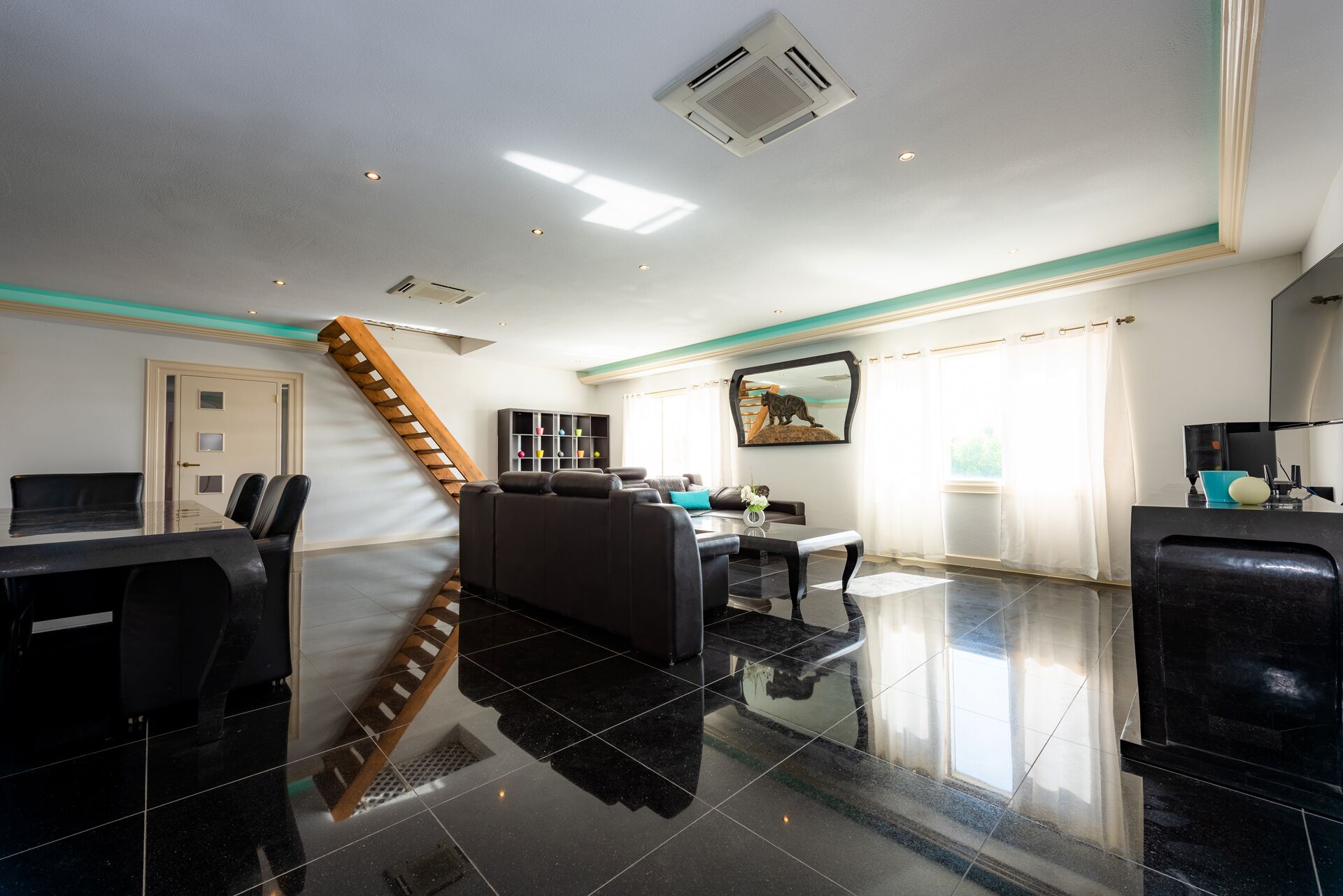 A modern hotel lobby with a staircase, a reception desk, a seating area, and a large window with curtains.