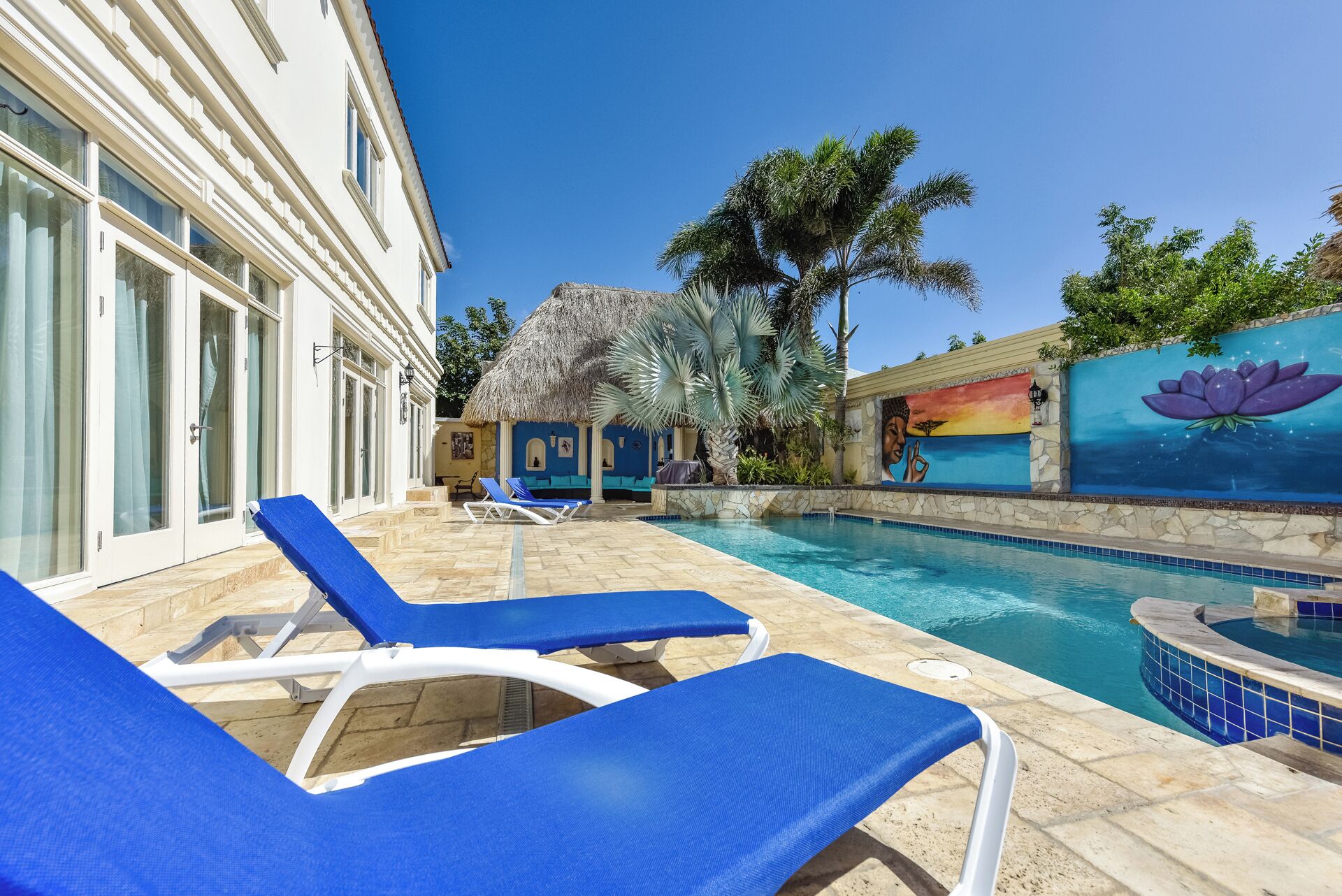 A pool area with blue lounge chairs, a stone pool, and a mural on the wall.
