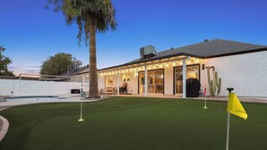 A backyard with artificial turf, a pool, and a house with a covered patio area. - The Dava | Free Heated Pool & Putting Green (Tempe)