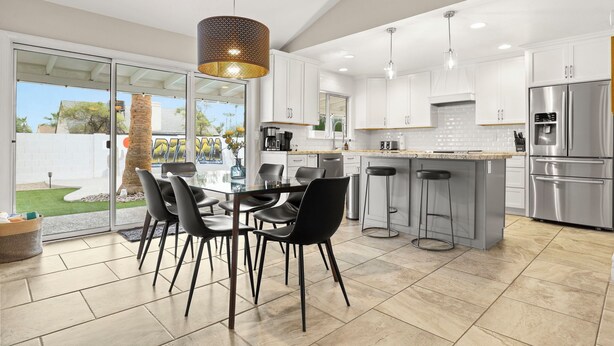 A modern kitchen with white cabinets, stainless steel appliances, and a dining area with black chairs and a glass table. - The Dava | Free Heated Pool & Putting Green (Tempe)