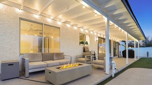 An outdoor patio with a fire pit, seating area, and a covered section with string lights. - The Dava | Free Heated Pool & Putting Green (Tempe)