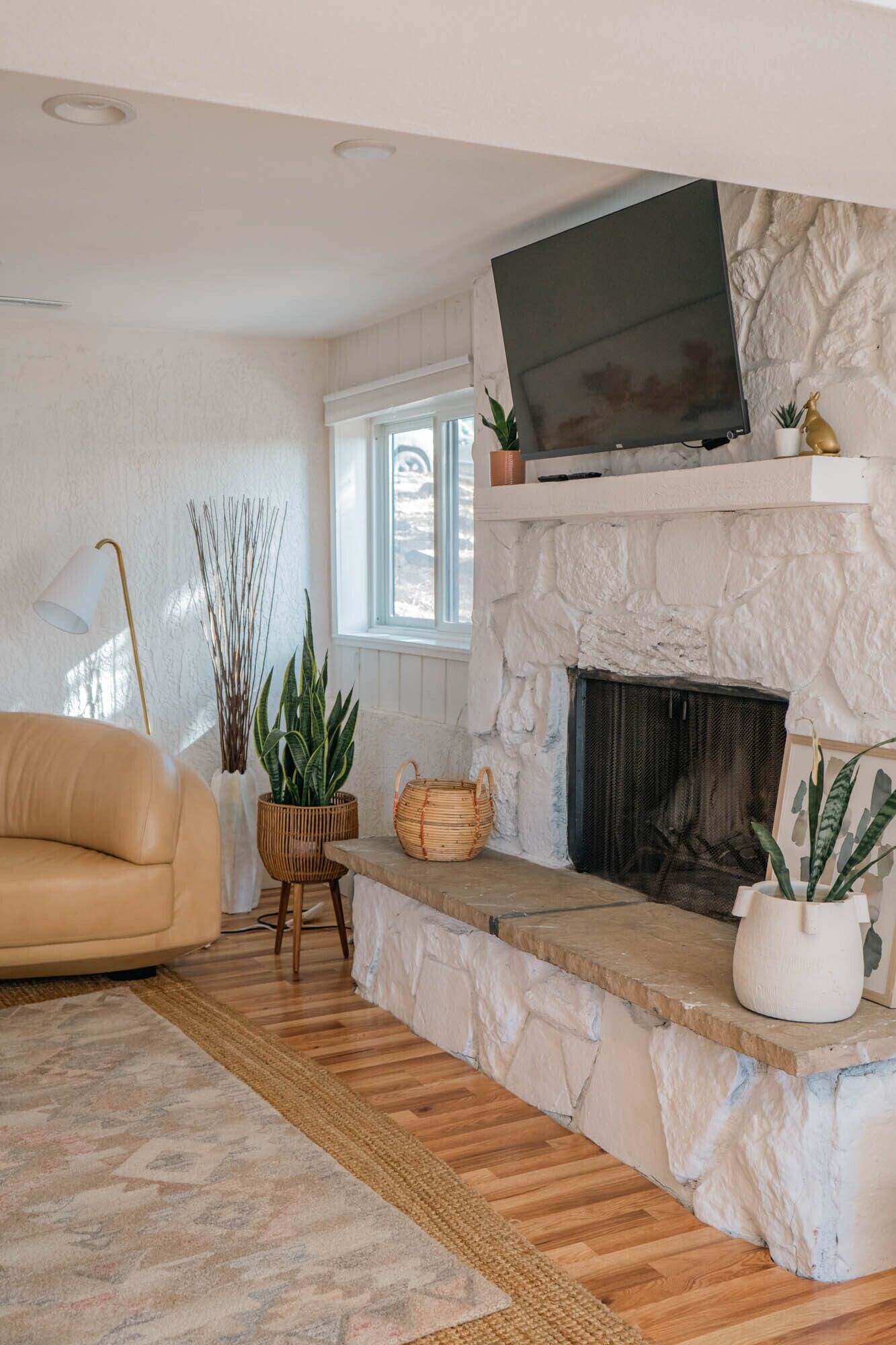 A living room with a stone fireplace, a television mounted above it, a sofa, and various plants.
