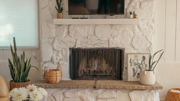 Una sala de estar con chimenea de piedra, un televisor de pantalla plana montado arriba y una mesa redonda de centro con un tapete tejido.