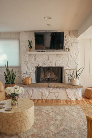 A living room with a stone fireplace, a flat-screen TV mounted above it, and a round coffee table with a woven rug. - Pikes Peak Mountain View 2 Bedroom Guest Suite (Colorado Springs)