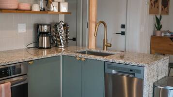 A compact kitchen with a built-in dishwasher, a coffee maker, and a sink with a gold faucet.