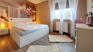Un dormitorio con cama, mesitas de noche, un radiador y cortinas traslúcidas.