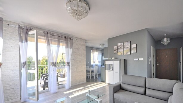 Una sala moderna con una mesa de centro de vidrio, sofá gris y un área de comedor al fondo.
