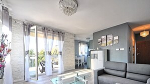Una sala de estar moderna con un sofá gris, una mesa de centro de vidrio y un comedor con una mesa y sillas blancas.