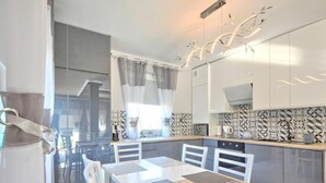 Una cocina moderna con armarios blancos, una mesa de comedor con cojines grises y azulejos de salpicadero con diseños.