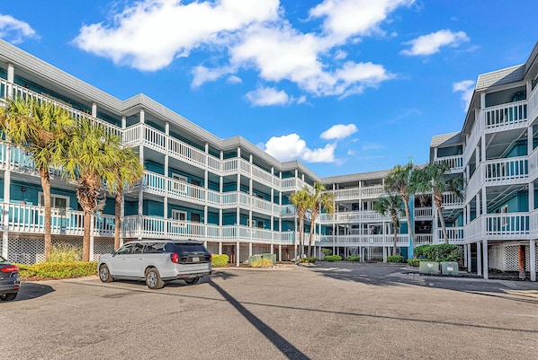 Un hôtel à plusieurs étages doté de balcons, d’un parking et de palmiers.