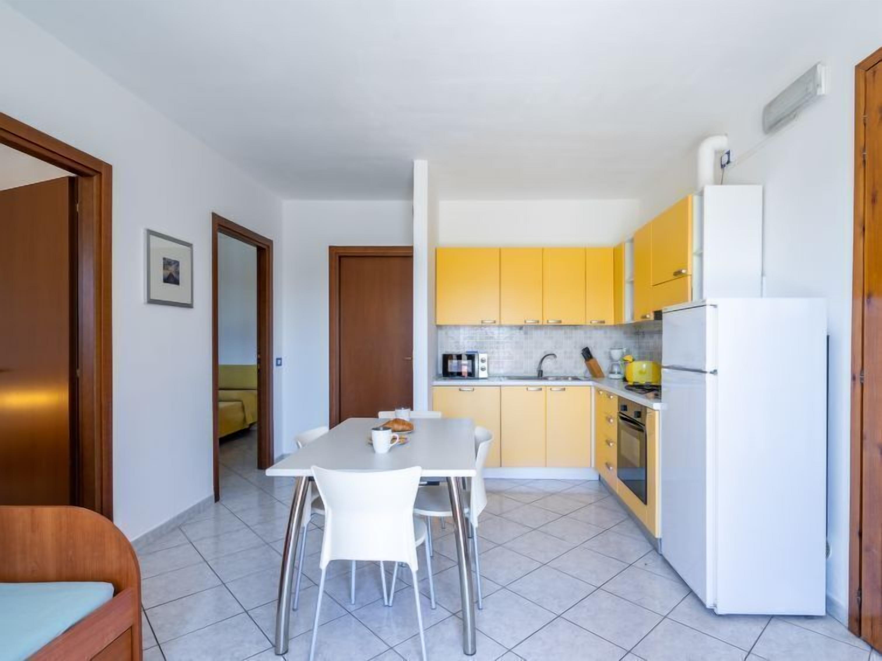 Eine kompakte Küche mit gelben Schränken, einem weißen Kühlschrank und einem Essbereich mit Tisch und Stühlen.