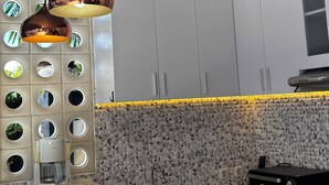 Moderni keittiö, jossa on puinen katto, riippuvalaisimet, kahvinkeitin ja sisäänrakennettu uuni.